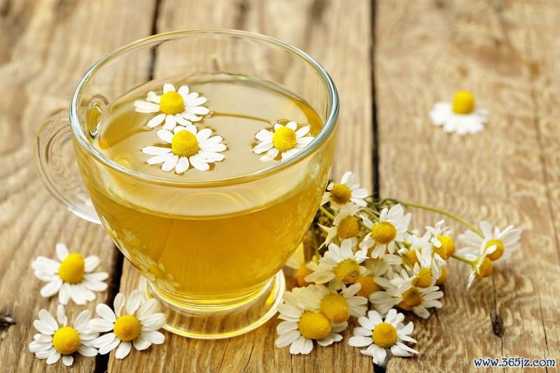 Herbal tea with lemon slice on a white wooden table with chamomile plants and cinnamon.